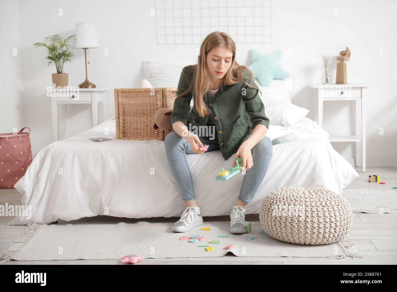 Müde junge Mutter, die im Schlafzimmer mit verstreuten Spielzeugen auf dem Boden ruhte Stockfoto