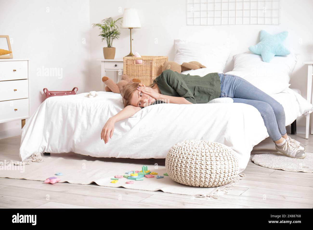 Müde junge Mutter, die im Schlafzimmer mit verstreuten Spielzeugen auf dem Boden ruhte Stockfoto