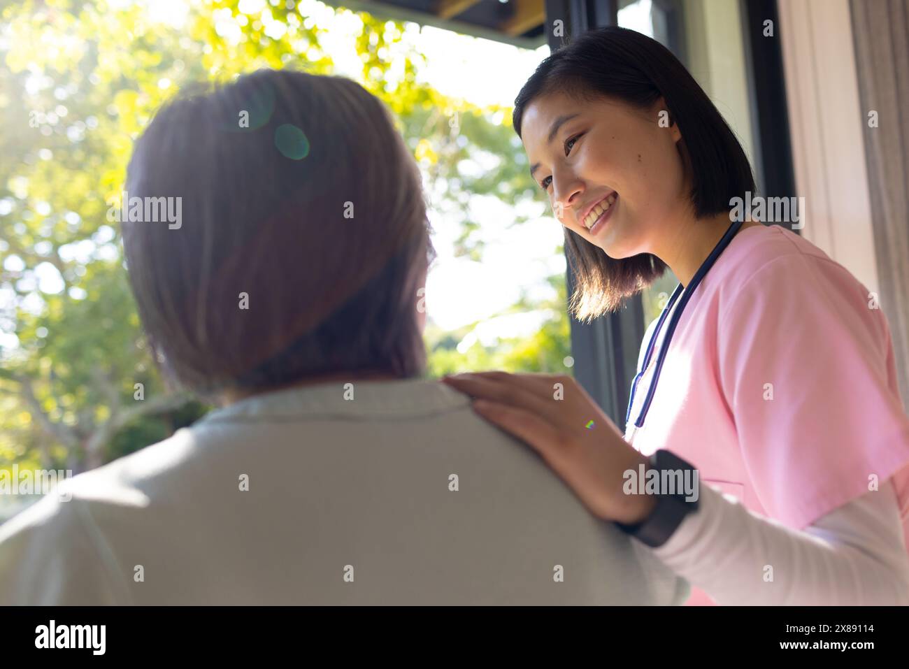 Zu Hause, asiatische junge Krankenschwester, die die Schulter des Patienten berührt Stockfoto