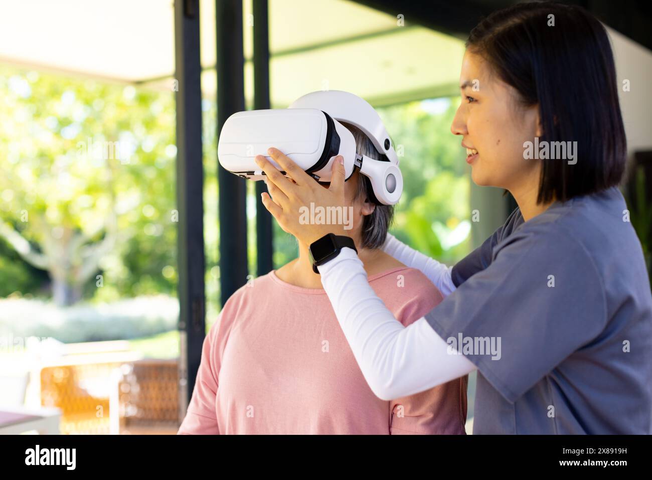 Zu Hause passen junge asiatische Krankenschwester und Patienten mittleren Alters das VR-Headset an Stockfoto