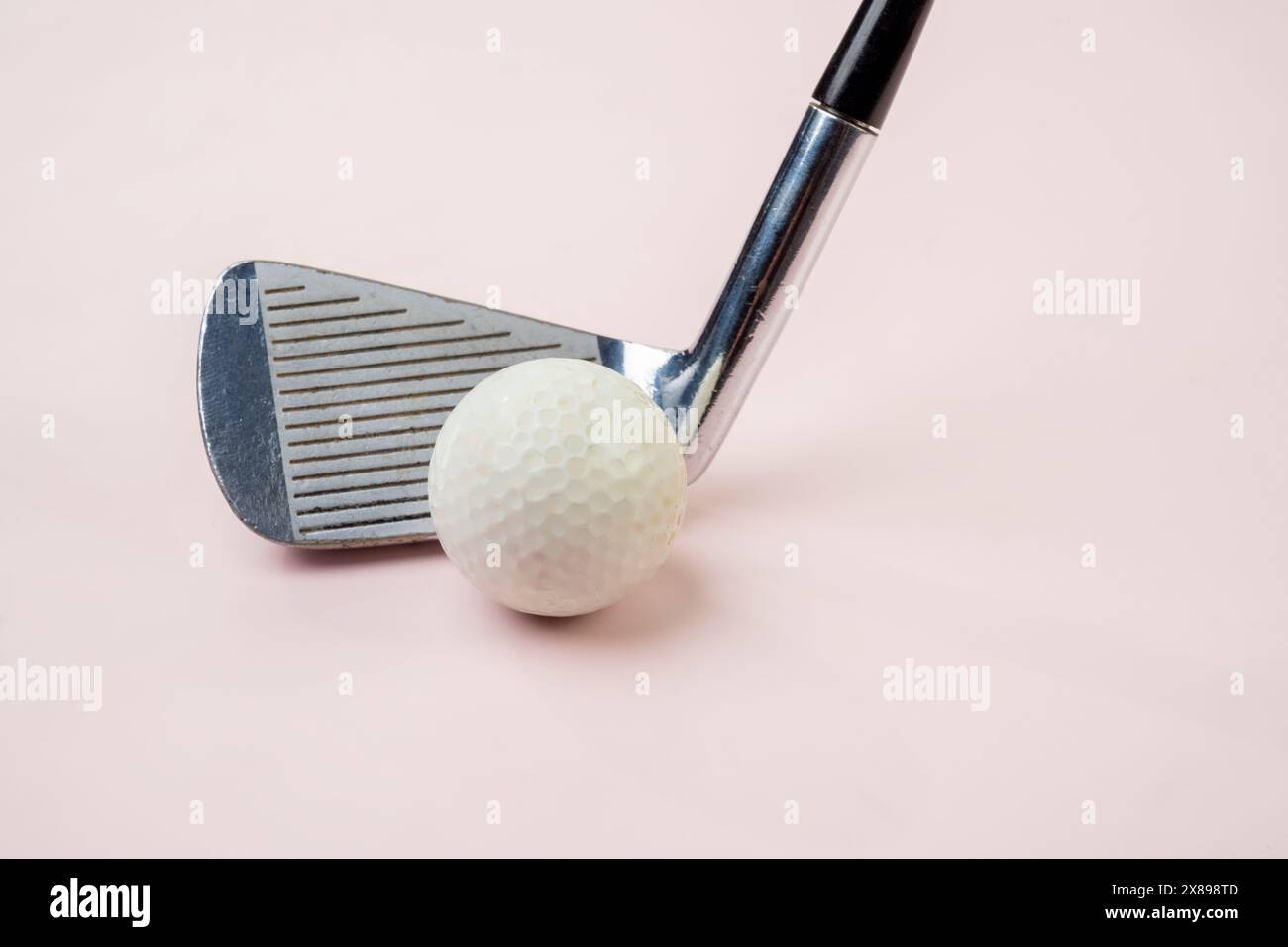 Nahaufnahme eines Golfschlägers und eines weißen Golfballs vor einem sanften rosafarbenen Hintergrund, das einen minimalistischen und modernen Ansatz für Sportausrüstung darstellt Stockfoto