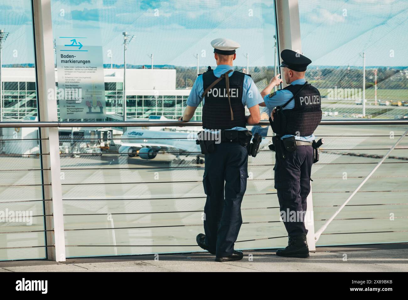 Zwei bewaffnete Flughafenpolizisten beobachten einen Rollweg am Flughafen München, Deutschland, von der Aussichtsplattform des Terminals 2 aus Stockfoto Zwei bewaffnete Flughafenpolizisten beobachten einen Rollweg am Flughafen München, Deutschland, von der Aussichtsplattform des Terminals 2 aus Stockfoto