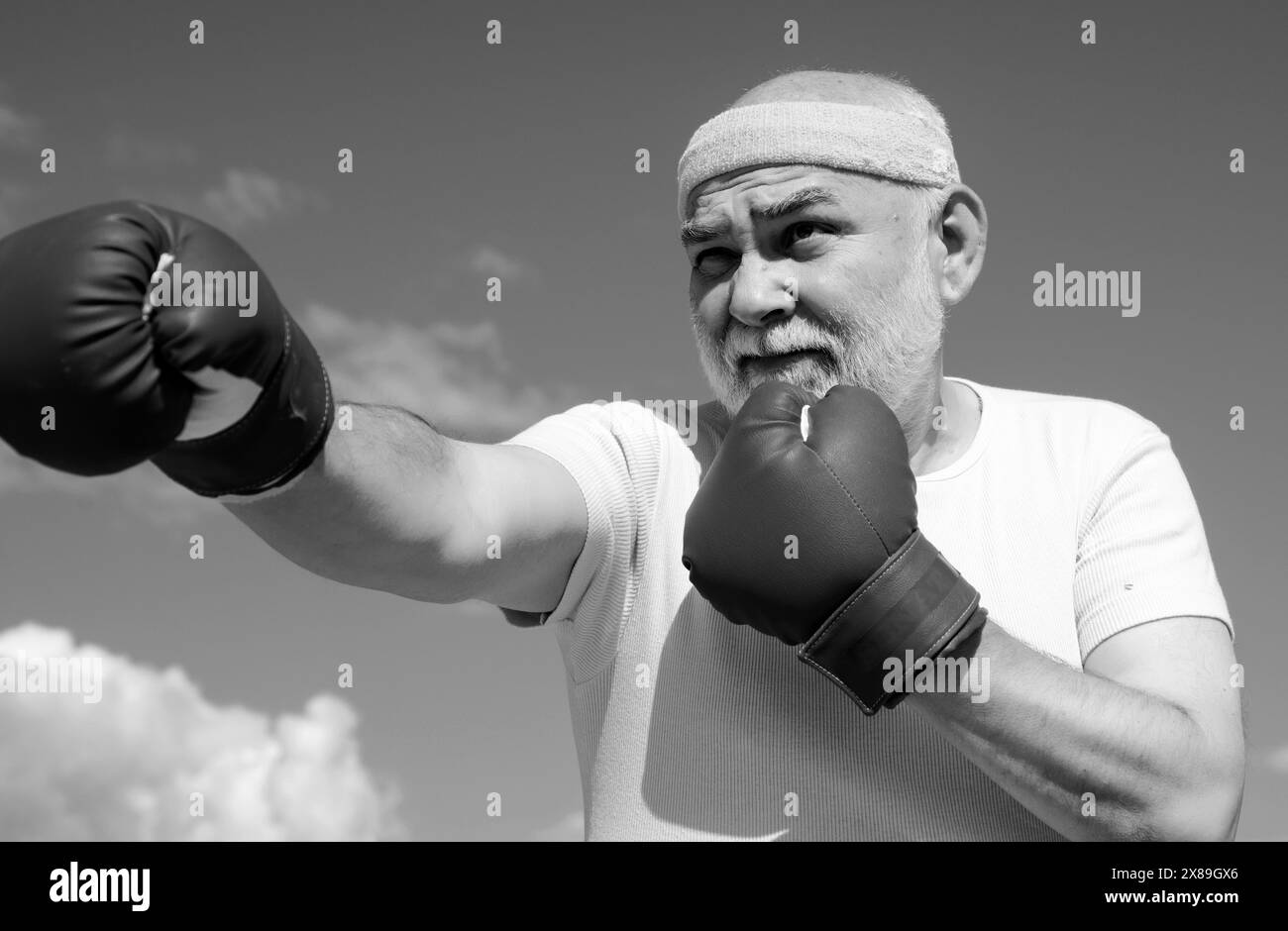 Schöner älterer Mann, der Boxtritte übt. Ein älterer Mann schlägt einen Boxsack. Ältere Männer kämpfen gegen Posen. Senior Sportmann mit Boxhandschuhen. Stockfoto