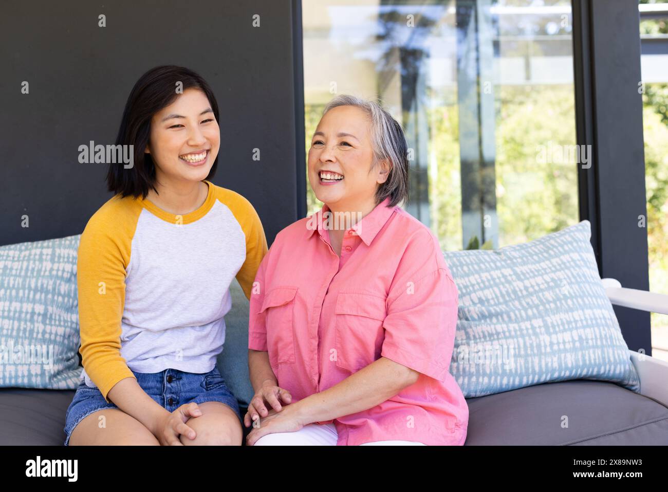 Zu Hause sitzen asiatische Mutter und Tochter mittleren Alters und lächeln zusammen Stockfoto