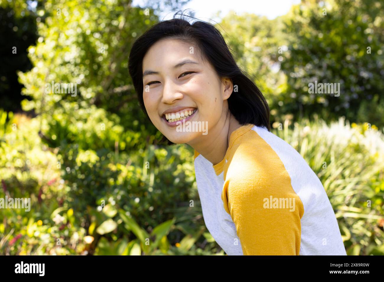 Asiatische junge Frau lächelt und trägt draußen gelbes Oberteil Stockfoto