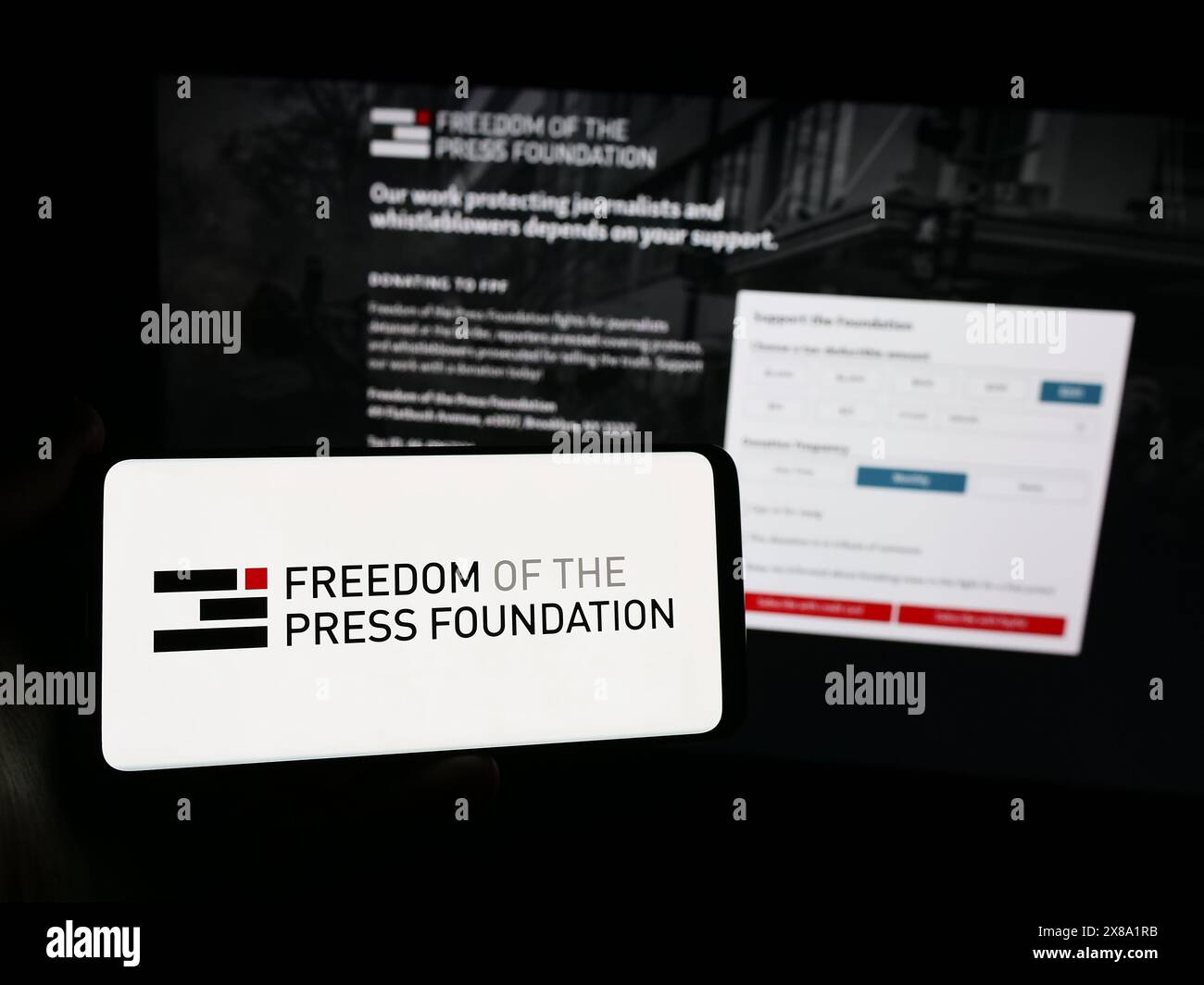 Person, die ein Smartphone mit dem Logo der Organisation Freedom of the Press Foundation (FPF) vor der Website hält. Schwerpunkt auf dem Display des Telefons. Stockfoto