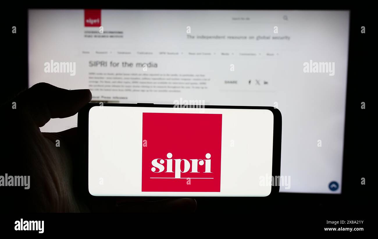 Person, die ein Mobiltelefon mit dem Logo des Stockholm International Peace Research Institute (SIPRI) vor der Webseite hält. Schwerpunkt auf dem Display des Telefons. Stockfoto