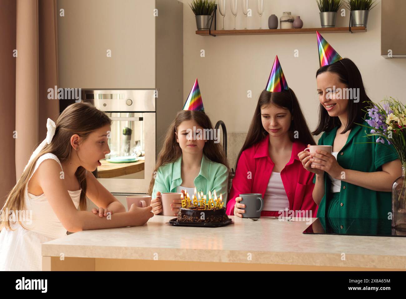 Vierköpfige Familie mit Partyhüten, die zu Hause einen Geburtstag mit Kuchen und Blumen feiern. Wichtige Momente, die das Feiern und die Familie in hervorheben Stockfoto