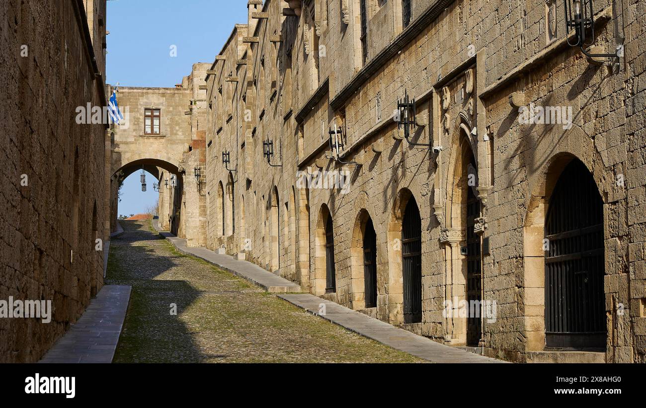 Eine historische Gasse mit Steinbauten und Bögen, blauen und weißen Fahnen im Hintergrund, Ritterstraße, Altstadt von Rhodos, Stadt Rhodos, Rhodos, Tun Stockfoto