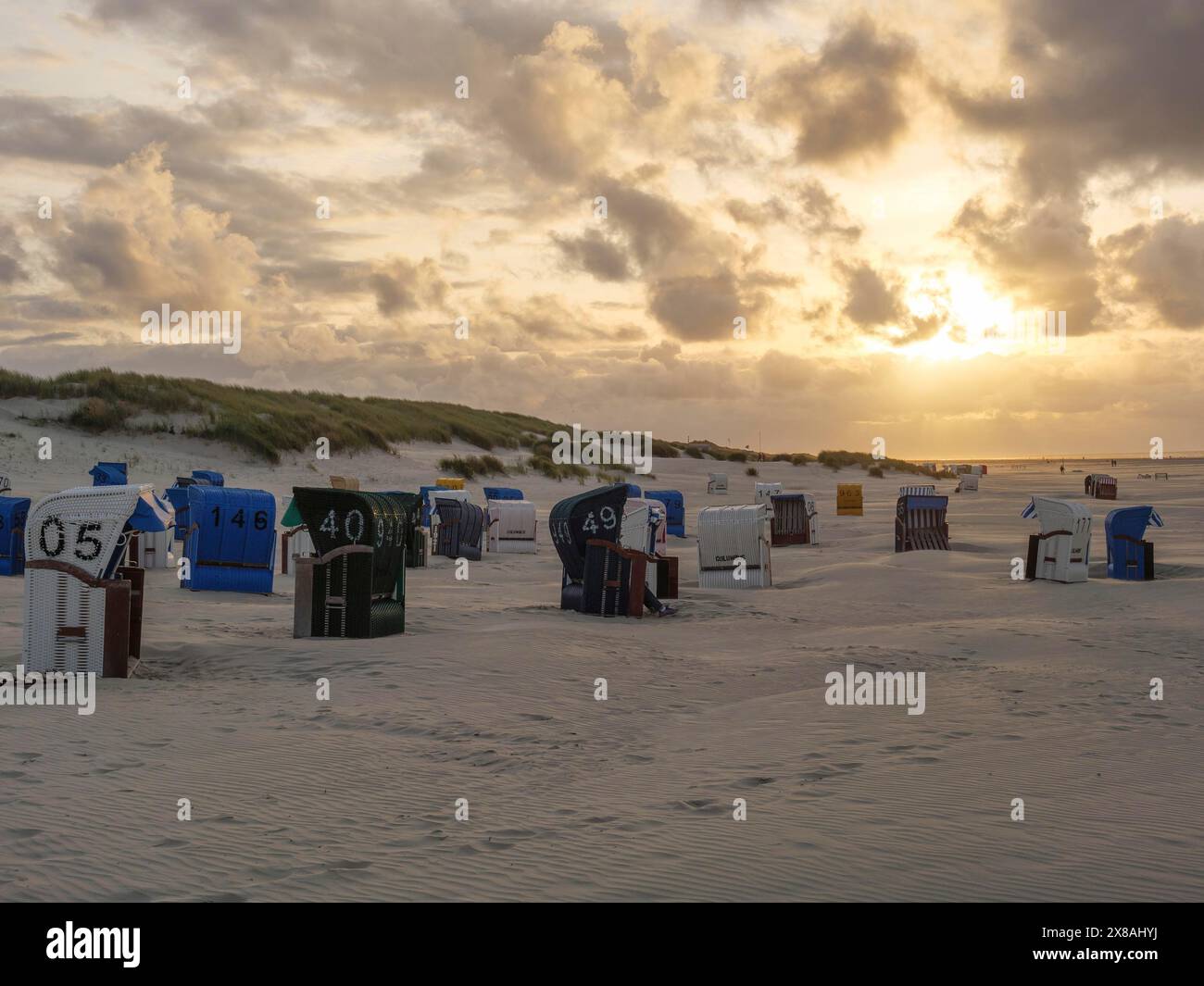 Liegestühle am Sandstrand bei Sonnenuntergang, umgeben von Dünen und bewölktem Himmel, Sommerabend am Nordsee mit einem schönen Sonnenuntergang am Strand Stockfoto