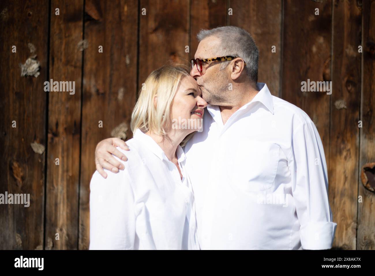 Senior Pärchen in weiß, die eine liebevolle Umarmung teilen Stockfoto