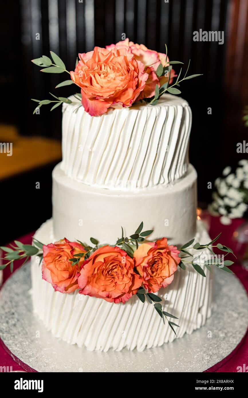 Zweischichtige weiße Hochzeitstorte mit orangen Rosen und grünen Blättern Stockfoto