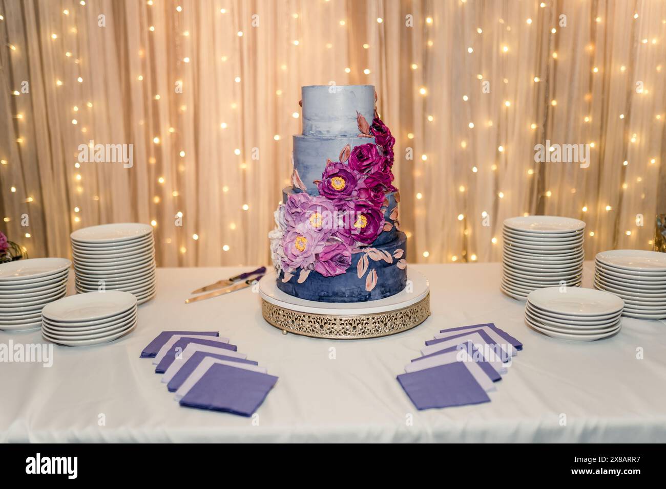 Dreistufige Hochzeitstorte mit lila Blumenschmuck auf einem Tisch Stockfoto