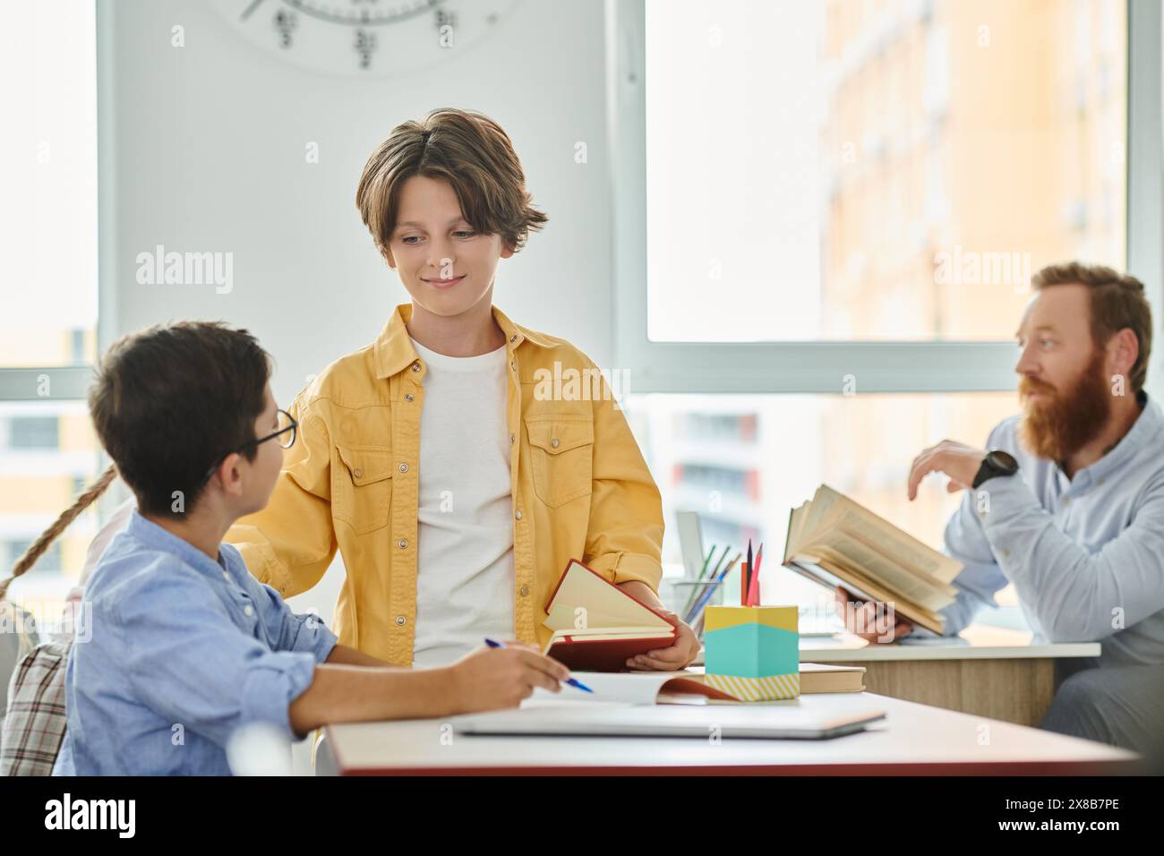 Eine Gruppe von Einzelpersonen, darunter ein Lehrer, ist vertieft in das gemeinsame Lernen von Büchern an einem hell erleuchteten Klassentisch. Stockfoto