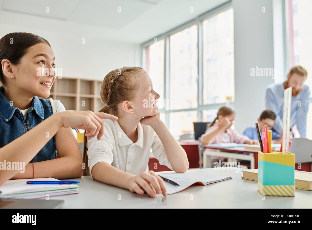 Zwei Mädchen, umgeben von Büchern und farbenfrohen Schulmaterialien, nehmen aktiv an einer Unterrichtsdiskussion Teil Stockfoto
