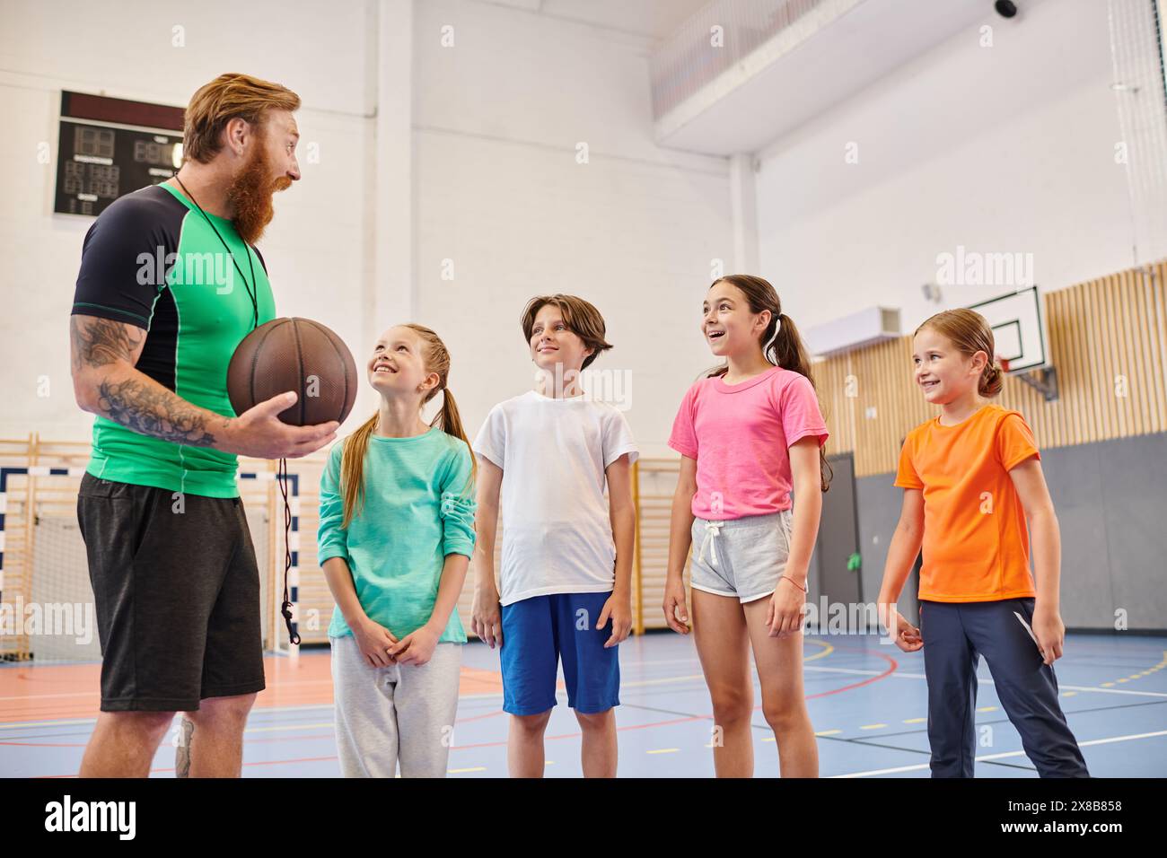 Ein Mann hält einen Basketball und führt eine vielfältige Gruppe von Kindern in einem lebhaften Klassenzimmer. Stockfoto