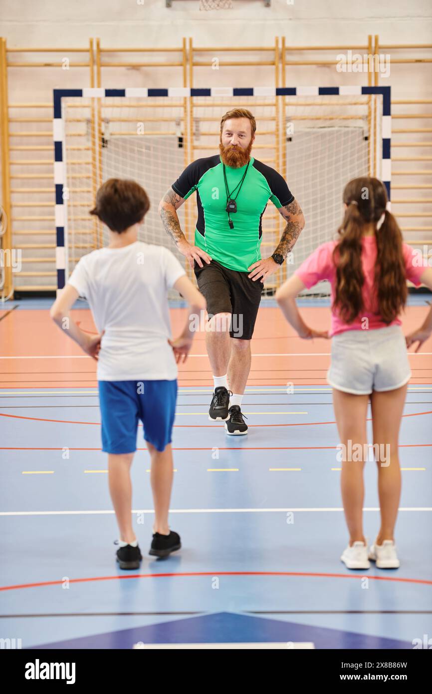 Eine vielfältige Gruppe von Kindern, geführt von einem männlichen Lehrer, trainieren gemeinsam auf einem hell beleuchteten Fitnessraum. Stockfoto