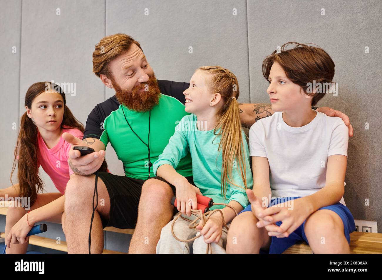 Ein Mann sitzt ruhig auf einer Bank, umgeben von aufmerksamen Kindern, in einem Moment tiefer Verbundenheit und Lernen. Stockfoto