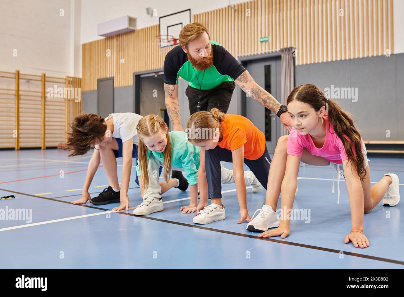 Eine Gruppe von Kindern nimmt an einer synchronisierten Liegestützsitzung auf einem Fitnessraum Teil, die von ihrem Lehrer geführt wird. Stockfoto