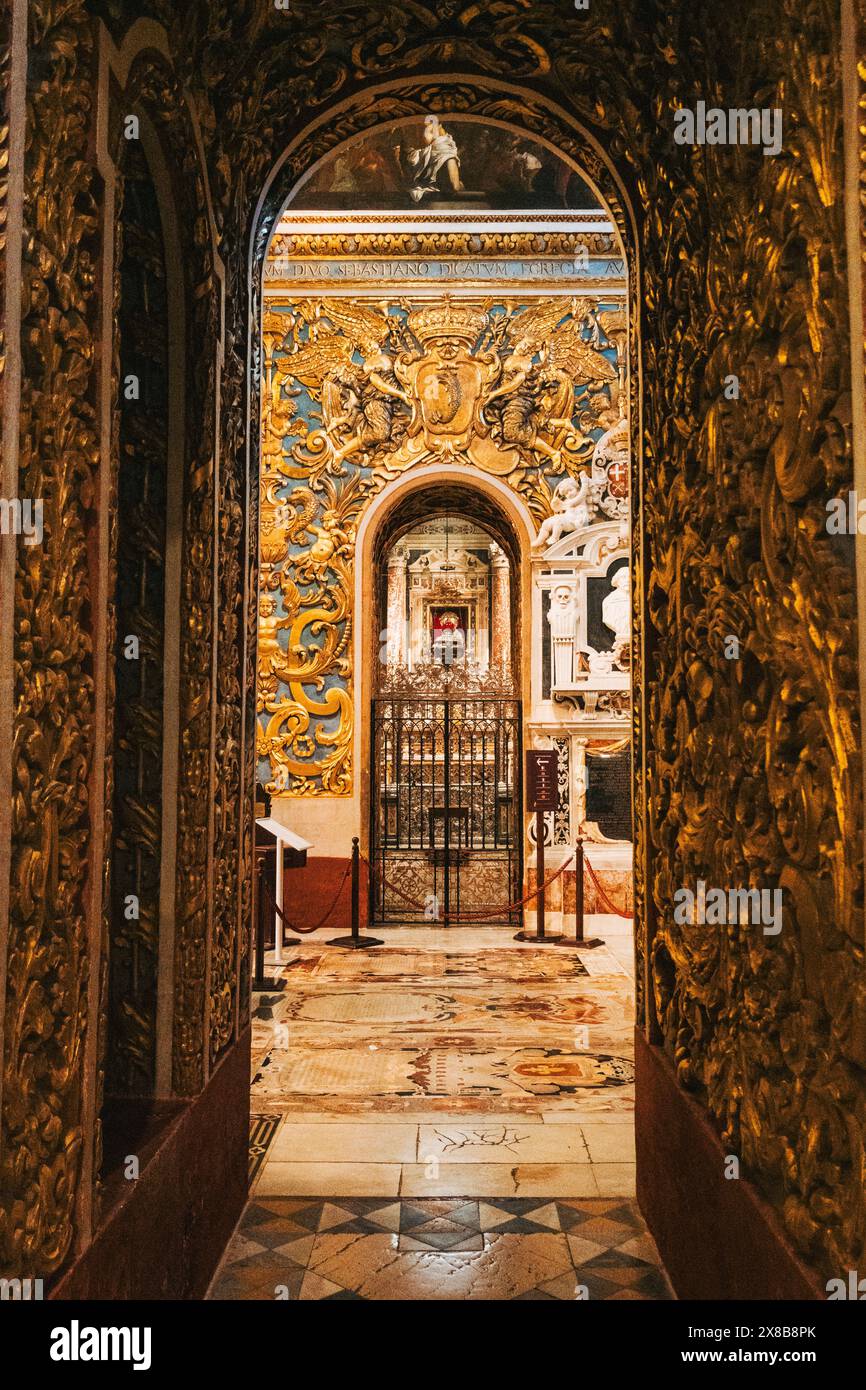 Ein Blick durch einen vergoldeten Bogengang führt zu einer Kapelle in einer Kathedrale in Malta, die komplizierte Schnitzereien und kunstvolle Details enthüllt. Stockfoto