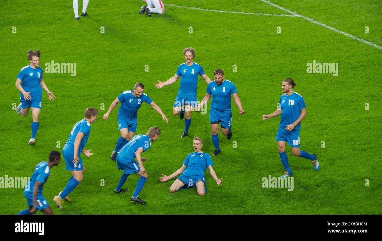 Meisterschaftsspiel: Blue Soccer Team Attack, Player Run Happy After Scoring Goal, Celebre Victory, doing Knee Slide. Sport Channel Broadcast Tv Konzept. Stockfoto