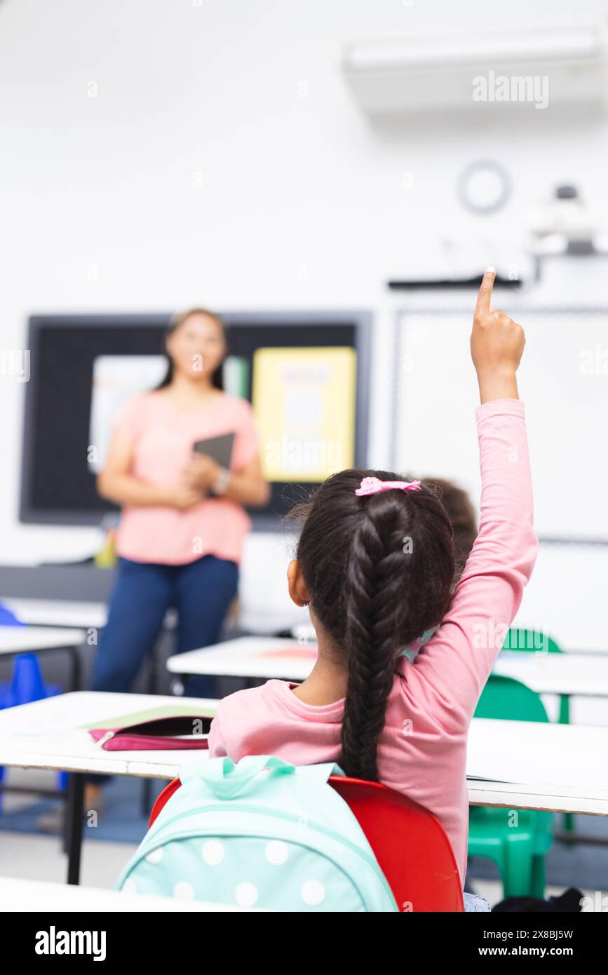 Eine birassische Lehrerin hält ein Tablet, die Schülerin hebt ihre Hand, Kopierraum Stockfoto