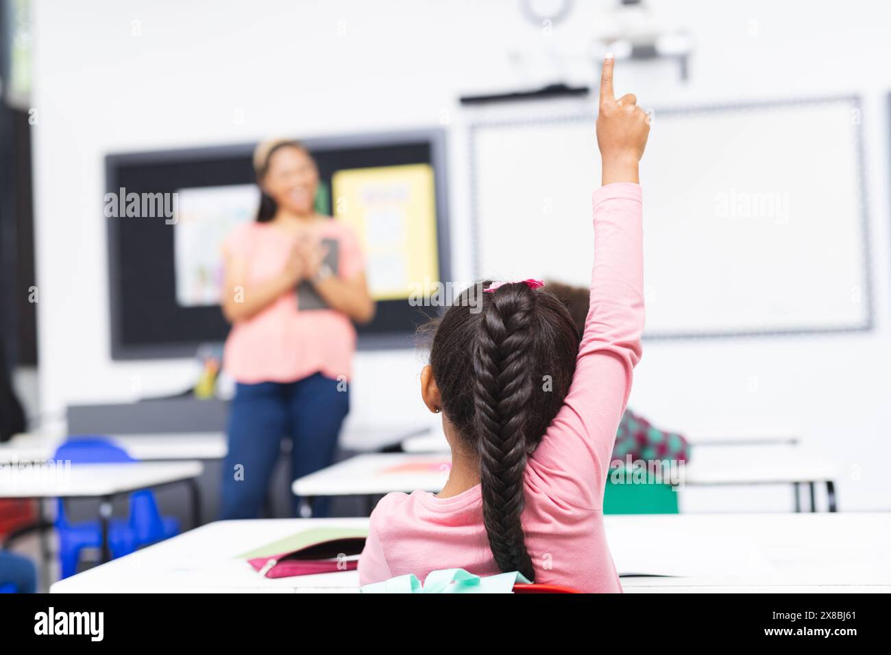 In der Schule, im Klassenzimmer, birassische junge Frau unterrichten, junges Mädchen hebt Hand Stockfoto