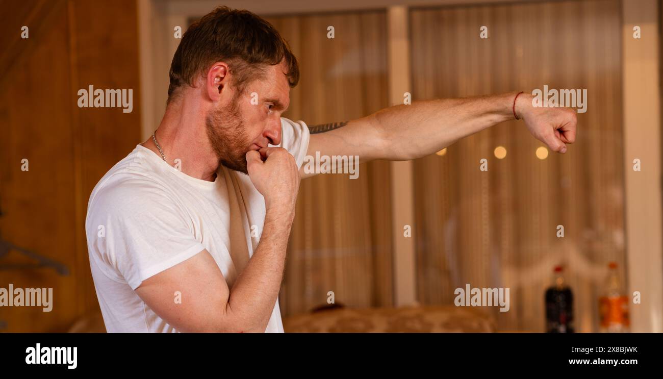 Ein Mann steht in einer Boxhaltung, mit einem ernsten Ausdruck. Er scheint bereit zu handeln und zeigt Durchsetzungskraft und Entschlossenheit Stockfoto Ein Mann steht in einer Boxhaltung, mit einem ernsten Ausdruck. Er scheint bereit zu handeln und zeigt Durchsetzungskraft und Entschlossenheit Stockfoto