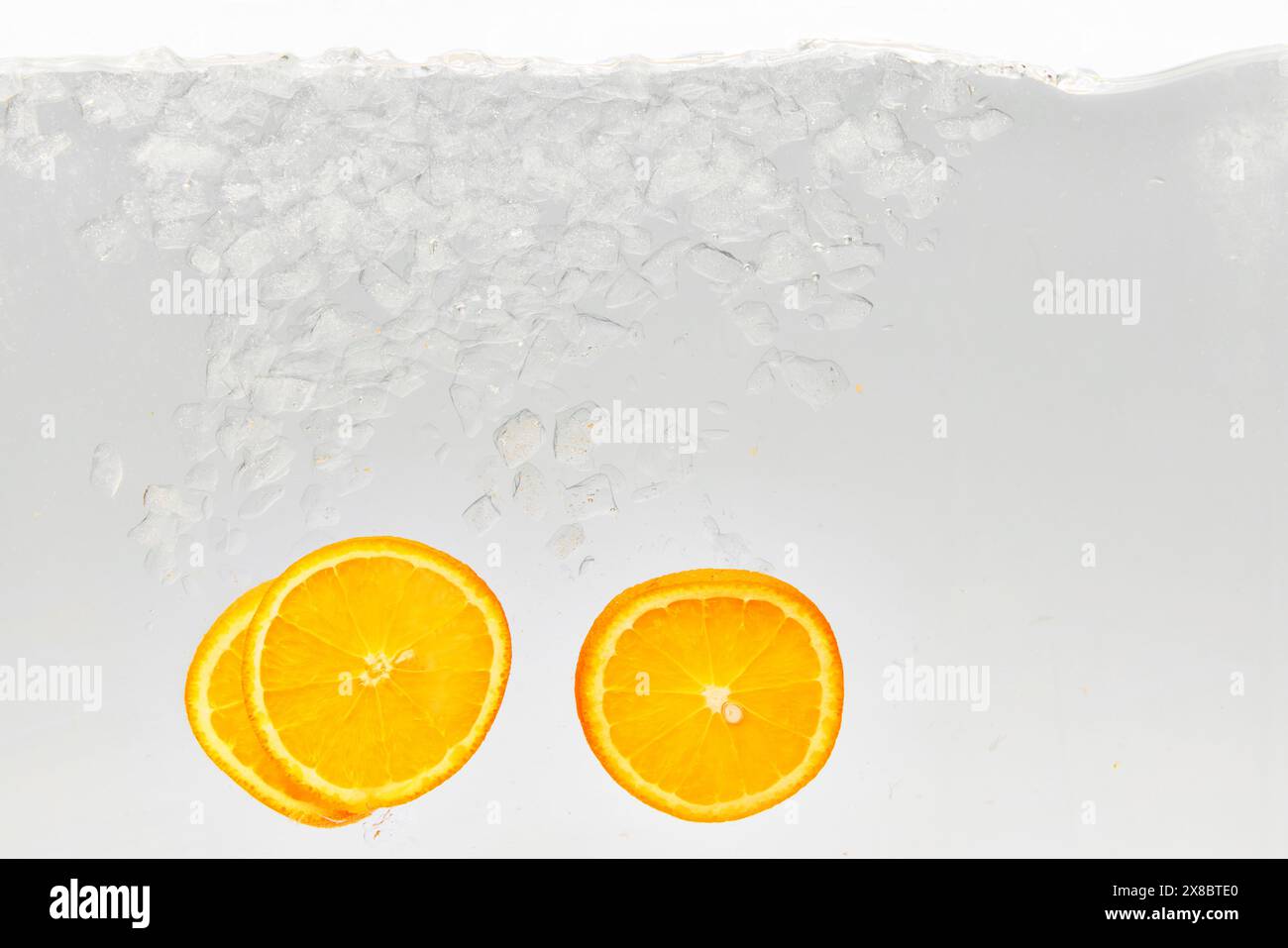 Strukturiertes Foto von einem Glas Wasser mit Eis, in dem Scheiben süße und saure Zitrusfrüchte, Orange, hinzugefügt werden. Abstraktes Hintergrundbild. Stockfoto