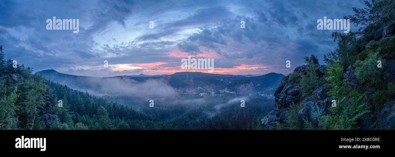 Nebel weht bergauf durch das Tal zu den Bergen. Die historische Burgruine und die barocke Bergkirche sind über dem Kurort Oybin zu sehen. Stockfoto