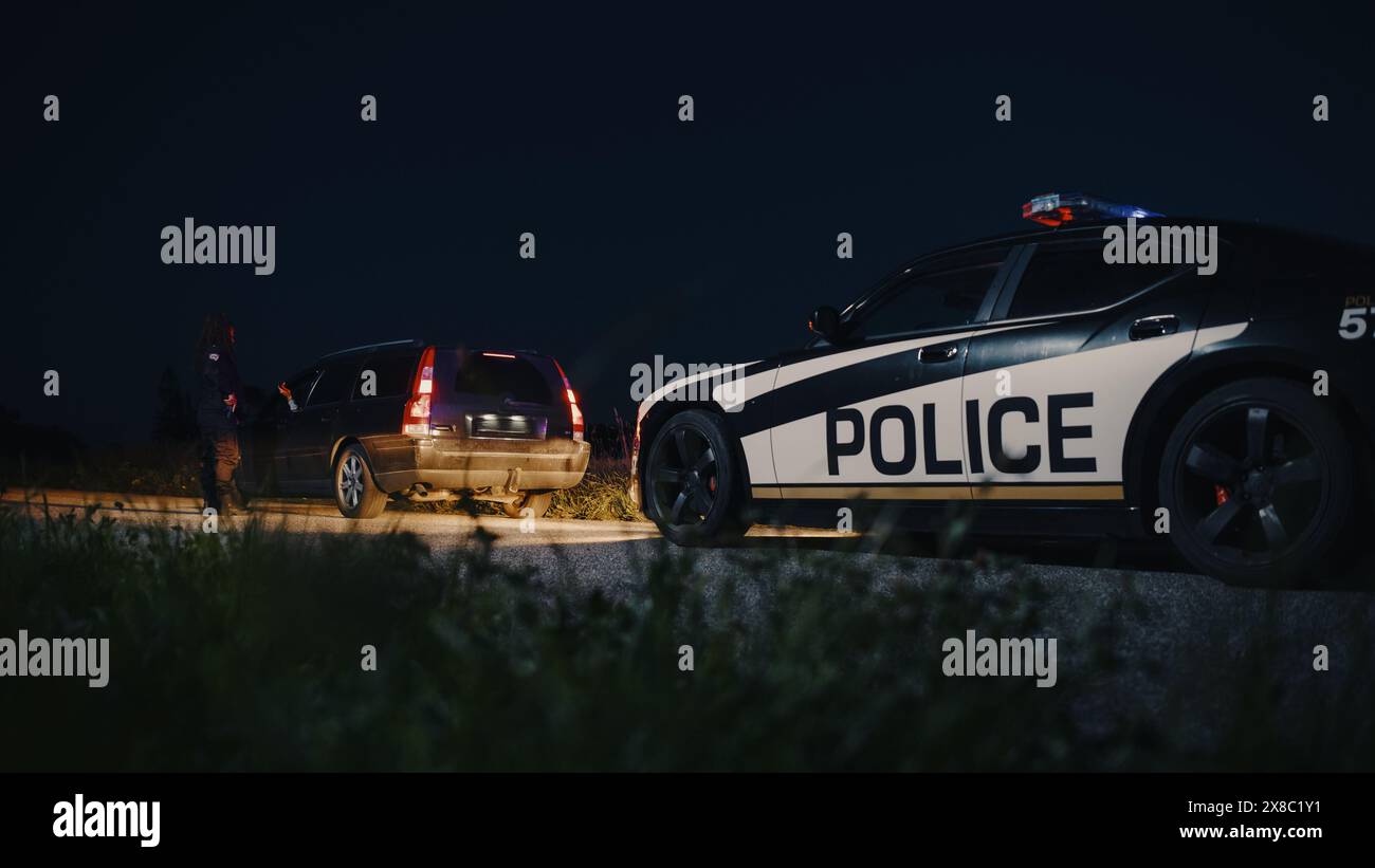 Schwarze Polizistin, die aus dem Patrouillenwagen steigt und auf ein angezogenes Auto zusteuert. Der Cop spricht mit dem Fahrer und stellt Fragen. Reguläre Papiere werden von der Strafverfolgungsbehörde überprüft Stockfoto