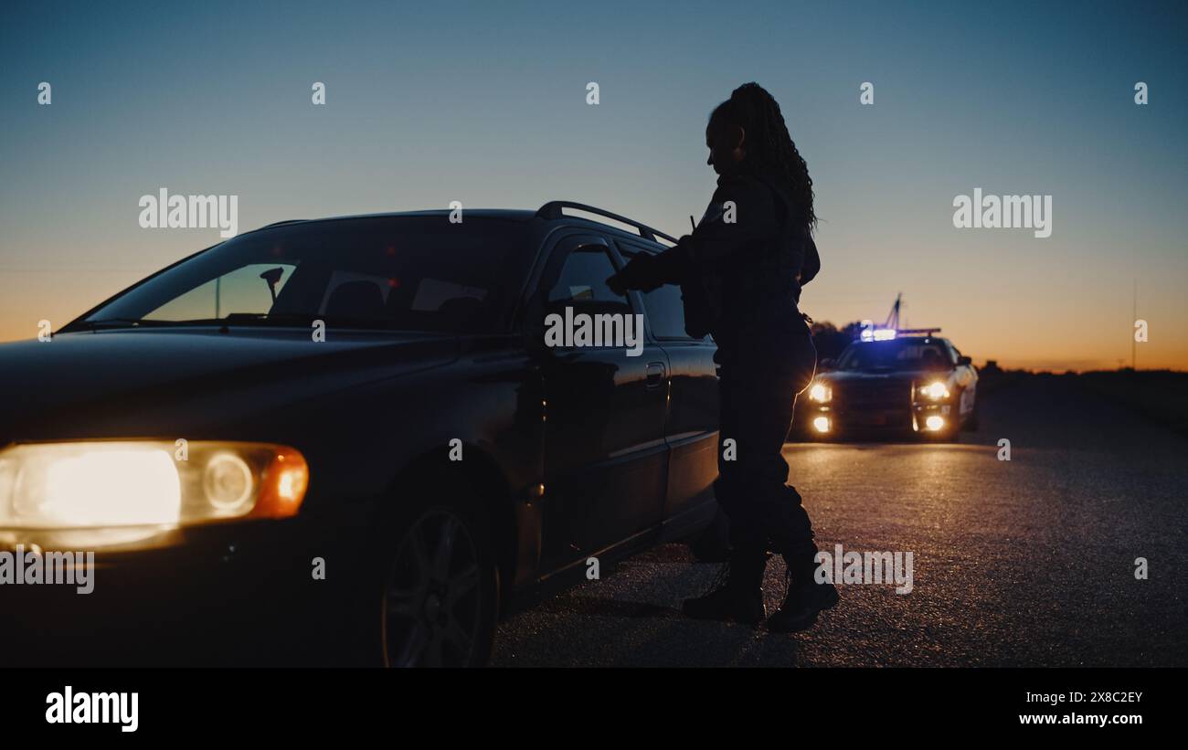 Schwarze Polizistin, die aus dem Patrouillenwagen steigt und auf ein angezogenes Auto zusteuert. Polizist klopft an das Fenster und befahl dem Fahrer, es herunterzurollen. Papiere Check durch die Strafverfolgungsbehörden Stockfoto