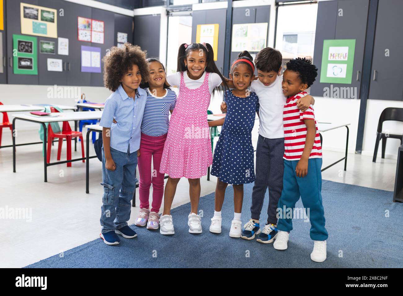 In der Schule umarmten sich sechs junge Schüler und lächelten im Klassenzimmer Stockfoto