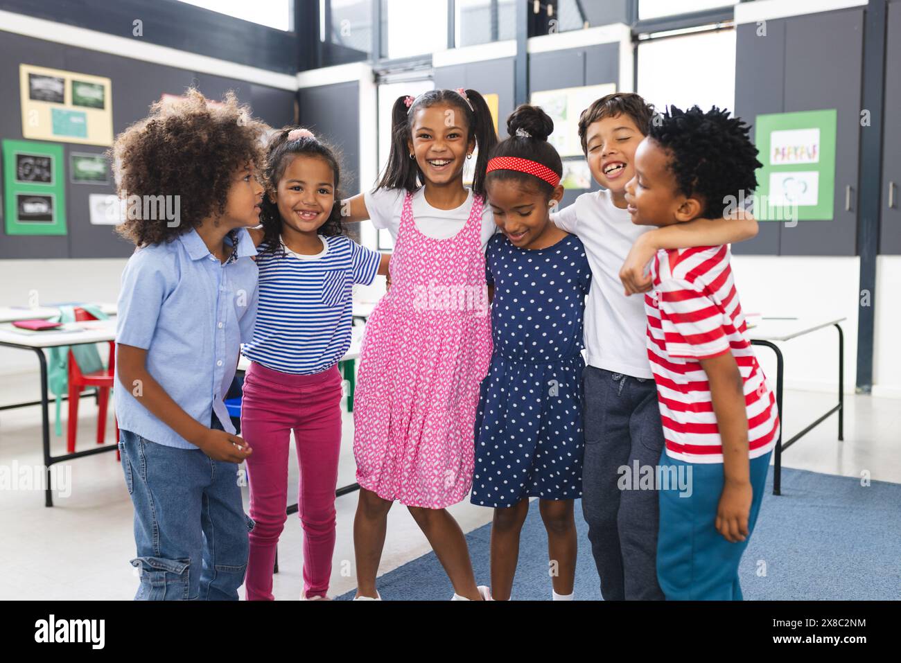 In der Schule umarmt und lacht eine Gruppe junger Schüler zusammen im Klassenzimmer Stockfoto