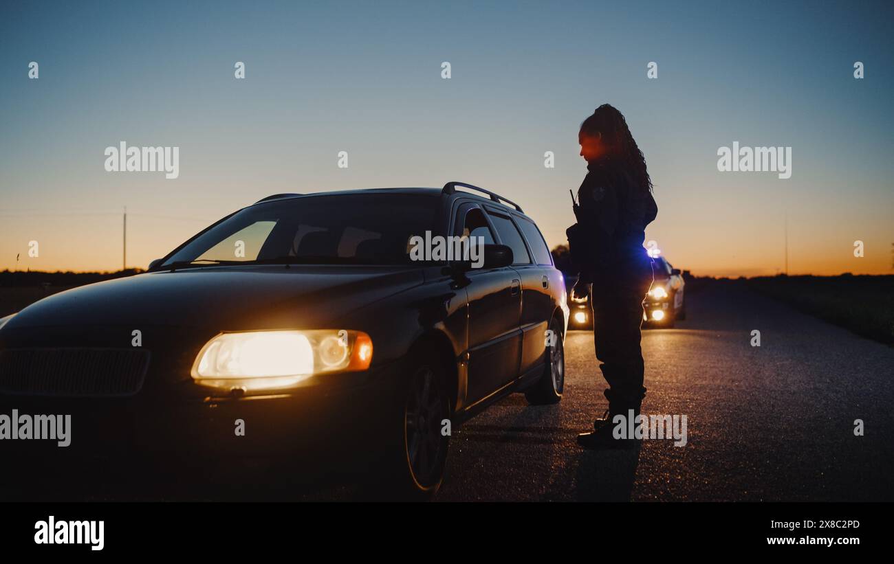 Schwarze Polizistin, die aus dem Patrouillenwagen steigt und auf ein angezogenes Auto zusteuert. Der Cop spricht mit dem Fahrer und stellt Fragen. Reguläre Papiere werden von der Strafverfolgungsbehörde überprüft Stockfoto