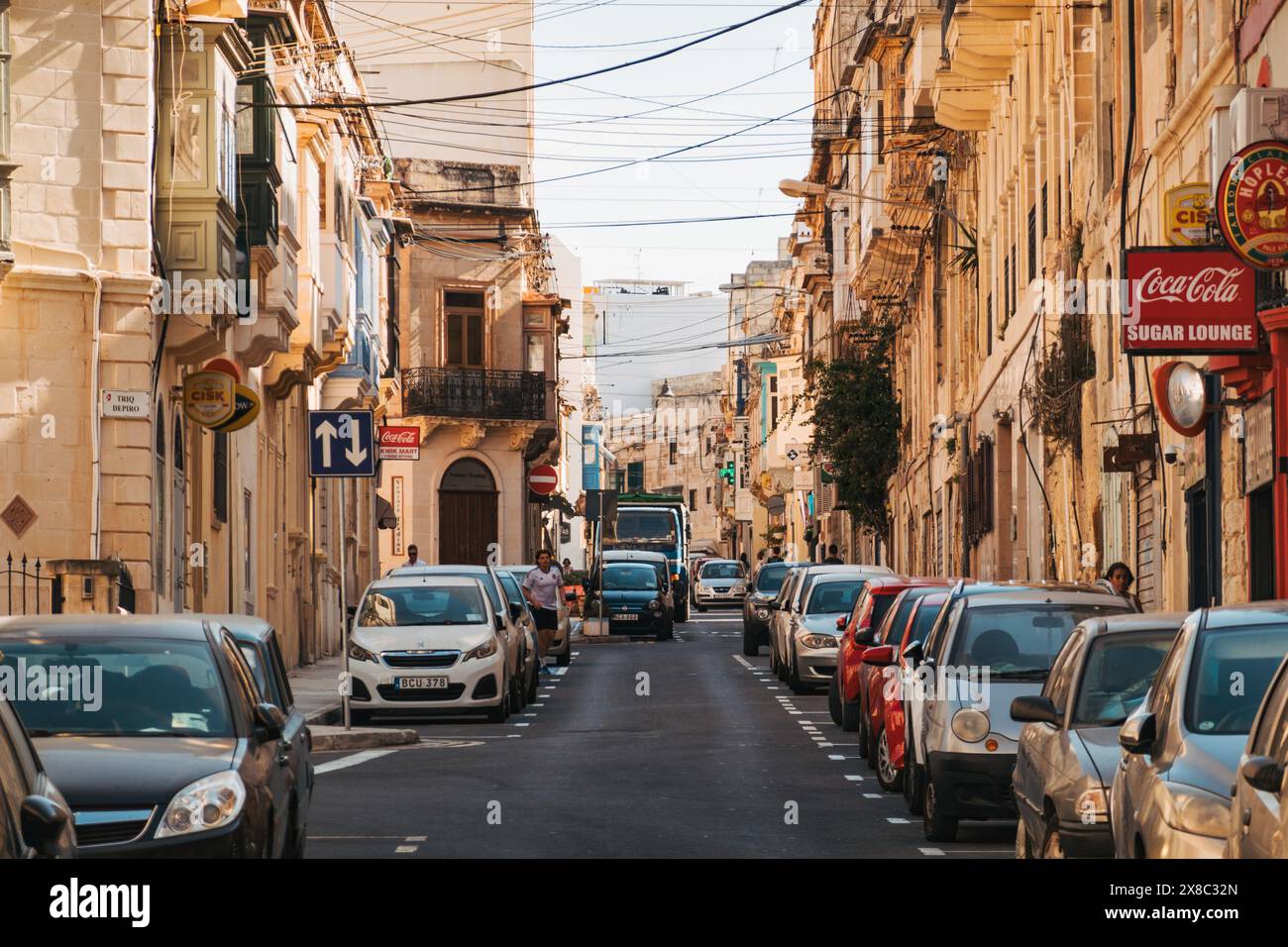 Kompakte Fahrzeuge parkten an einem sonnigen Nachmittag entlang einer engen Wohnstraße, die von Kalksteinbauten gesäumt ist, in der Stadt Sliema, Malta Stockfoto