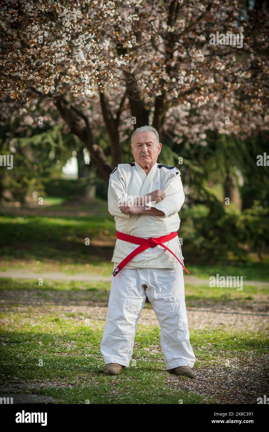 Ein Meister der Kampfkunst in einem traditionellen Gi-Kimono steht selbstbewusst in einem Park, mit überkreuzten Armen und strahlt Autorität und Expertise in Judo, Aikido und Jiu-jits aus Stockfoto