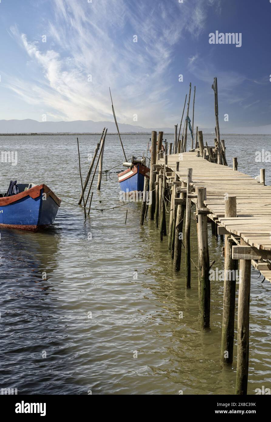 Ein verwitterter hölzerner Pier und eine kleine Hütte erstrecken sich in einen ruhigen Fluss, in dessen Nähe ein einsames Boot ankert. Stockfoto