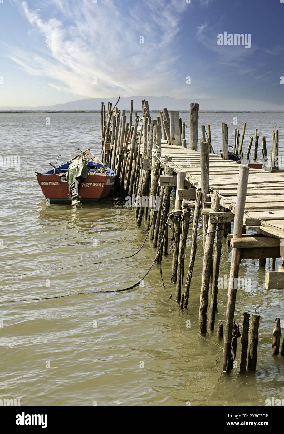 Ein verwitterter hölzerner Pier und eine kleine Hütte erstrecken sich in einen ruhigen Fluss, in dessen Nähe ein einsames Boot ankert. Stockfoto