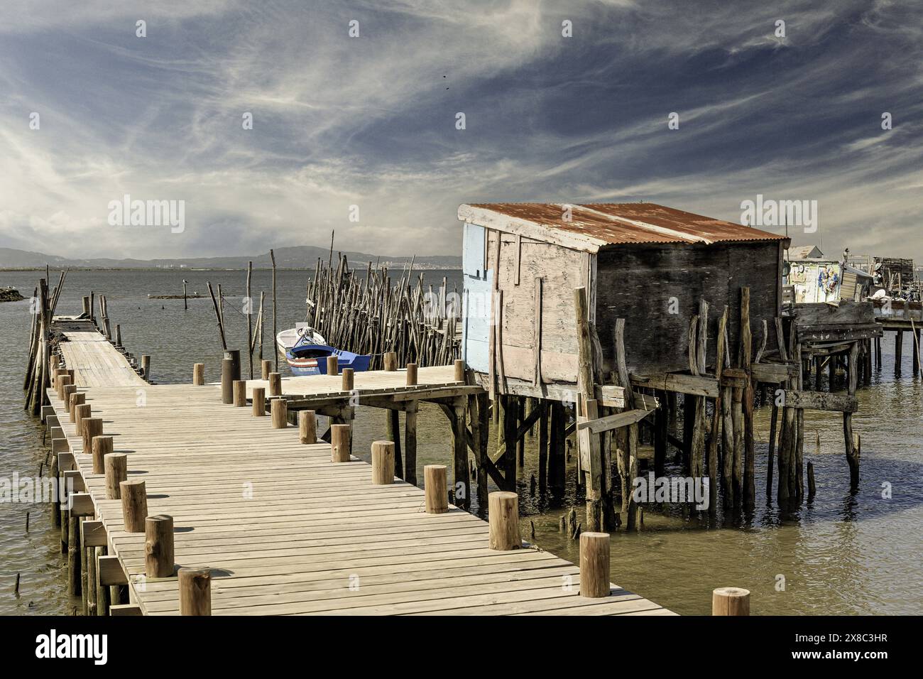 Ein verwitterter hölzerner Pier und eine kleine Hütte erstrecken sich in einen ruhigen Fluss, in dessen Nähe ein einsames Boot ankert. Stockfoto