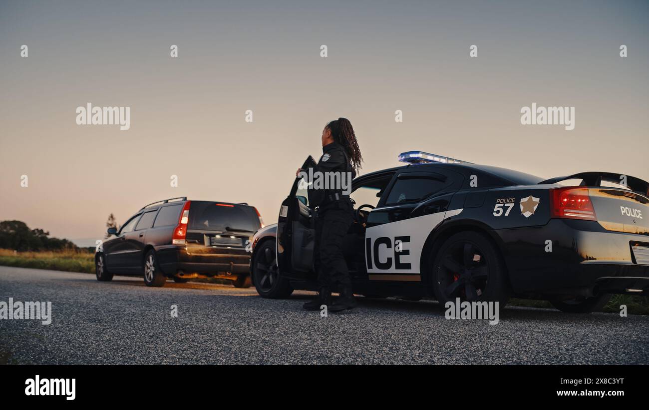 Schwarze Polizistin, die aus dem Patrouillenwagen steigt und auf ein angezogenes Auto zusteuert. Die Polizei antwortete auf einen Anruf von 911 wegen eines verdächtigen Autos, der auf der Straße angehalten wurde, und untersucht die Situation Stockfoto