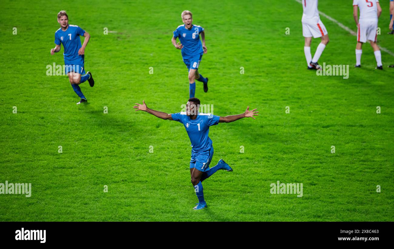 Meisterschaftsspiel: Blue Soccer Team Attack, Black Player Run Happy After Scoring Goal, Celebre Victory, schaut in die Kamera. Sport Channel Broadcast Tv Konzept. Stockfoto