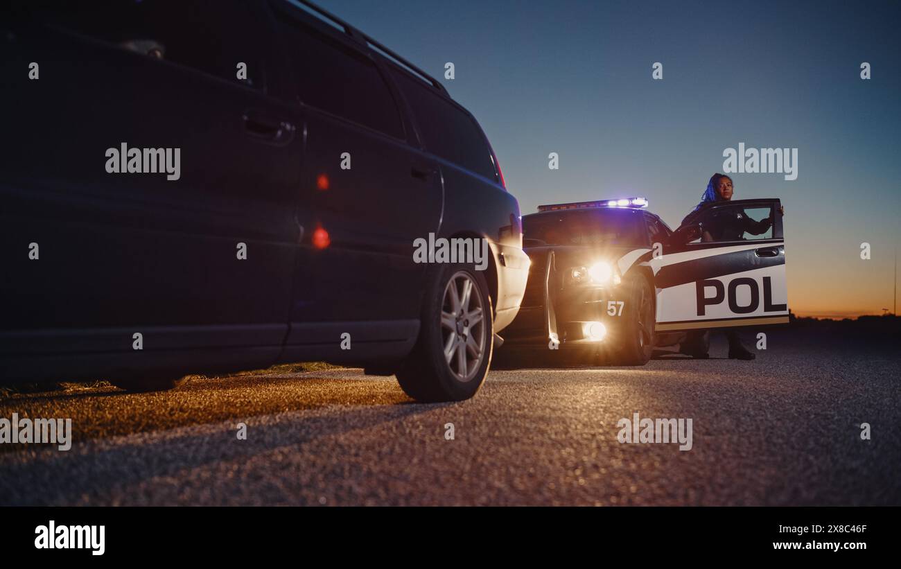 Schwarze Polizistin, die aus dem Patrouillenwagen steigt und auf ein angezogenes Auto zusteuert. Die Polizei antwortete auf einen Anruf von 911 wegen eines verdächtigen Autos, der auf der Straße angehalten wurde, und untersucht die Situation Stockfoto