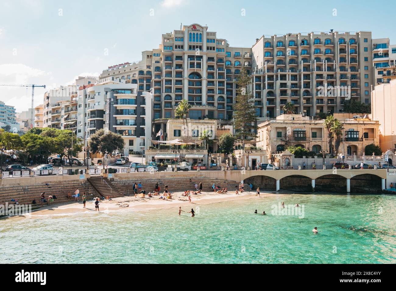 Die Menschen entspannen sich im flachen türkisfarbenen Wasser am wunderschönen Balluta Bay Beach in St. Julian's, Malta Stockfoto