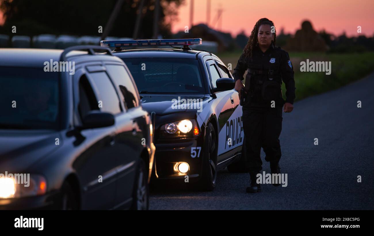 Der Highway Traffic Patrol Car fährt über das Fahrzeug auf der Straße. Die Polizistin kommt zu dem Fahrer und bittet um eine Lizenz und Registrierung. Schwarzer Offizier des Gesetzes, der beruflich Arbeit leistet. Seitliche Rückansicht Stockfoto