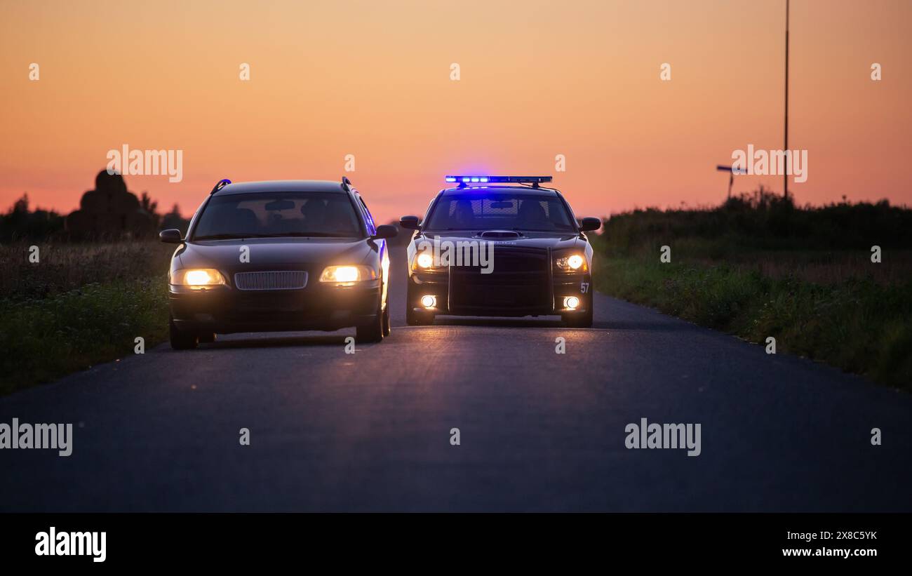 Der Highway Traffic Patrol Car fährt über das Fahrzeug auf der Straße. Der männliche Polizeibeamte kommt zu dem Fahrer und bittet um Lizenz und Registrierung, der schwarze weibliche Kollege deckt ihn ab. Weitwinkelaufnahme In Kinoqualität Bei Dämmerung Stockfoto