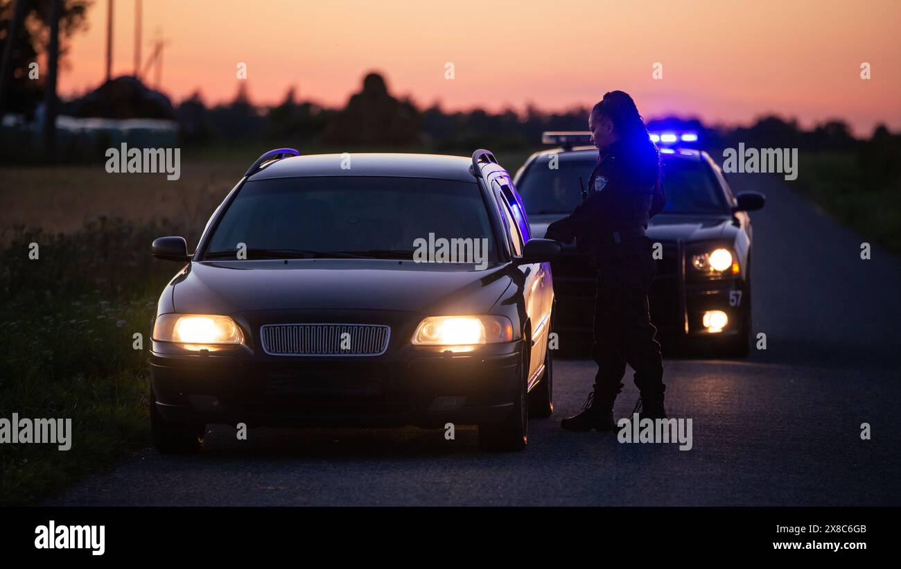 Der Highway Traffic Patrol Car fährt über das Fahrzeug auf der Straße. Die Polizistin kommt zu dem Fahrer und bittet um eine Lizenz und Registrierung. Schwarzer Offizier des Gesetzes, der beruflich Arbeit leistet. Seitliche Rückansicht Stockfoto