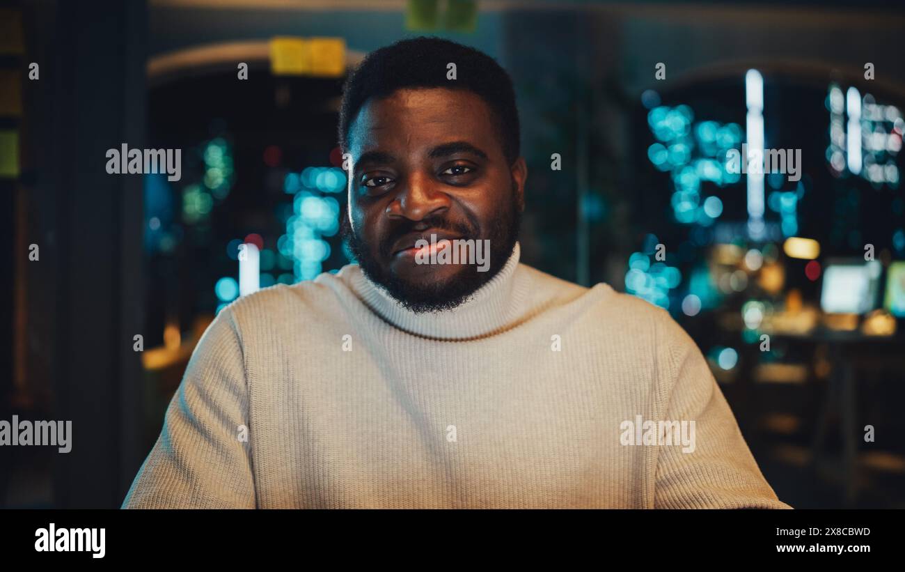 Blickwinkel aus der Kamera mit dem gutaussehenden Young Black Project Manager, der in einer abendlichen Büroumgebung ein Videogespräch führt. Afroamerikanischer männlicher Spezialist, der mit einem Kollegen über eine Live-Kamera spricht. Stockfoto