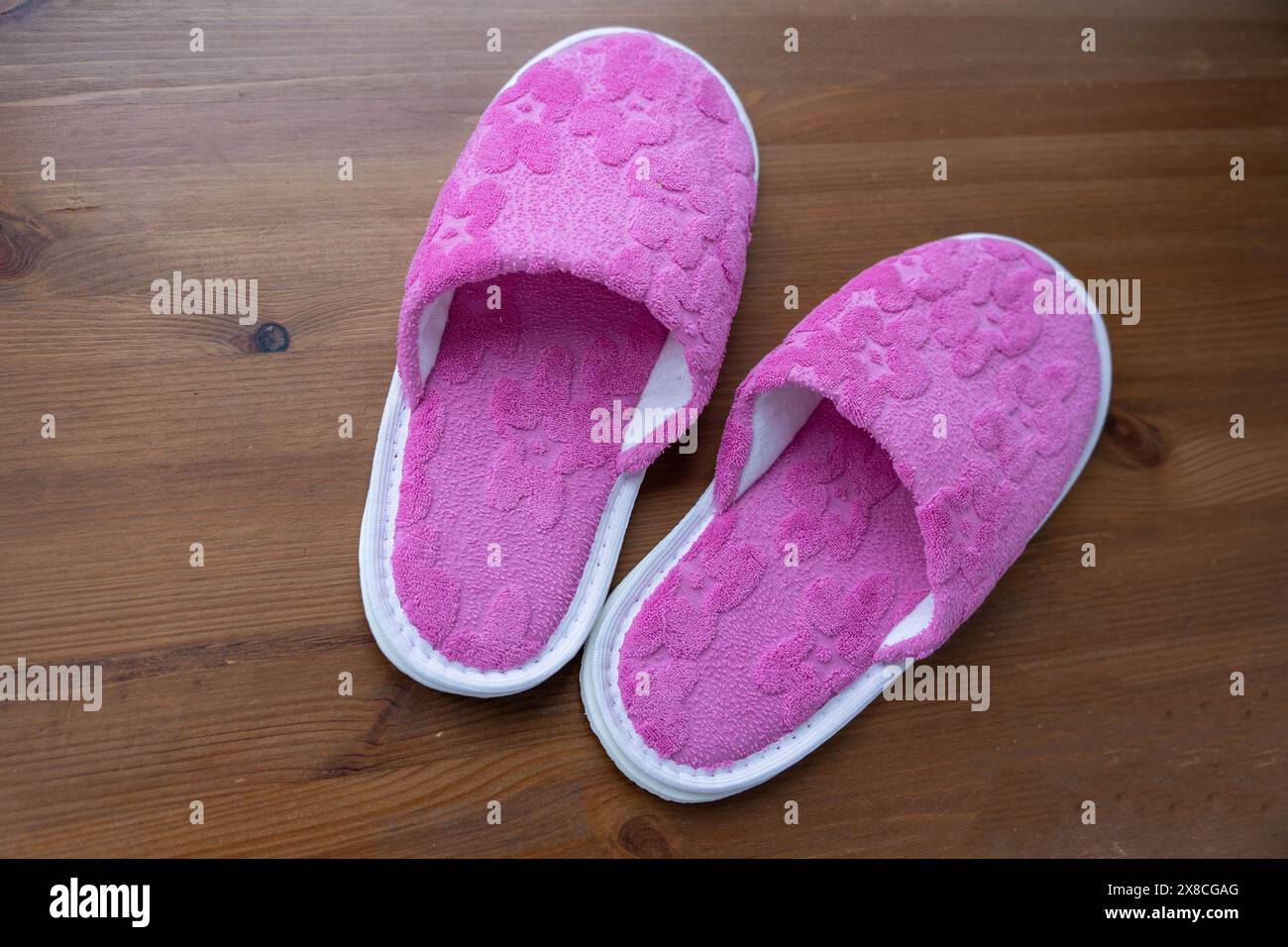 Ein Paar pinkfarbene Hausschuhe liegt auf einem Holzboden und sorgt so für eine einfache und gemütliche Szene. Stockfoto