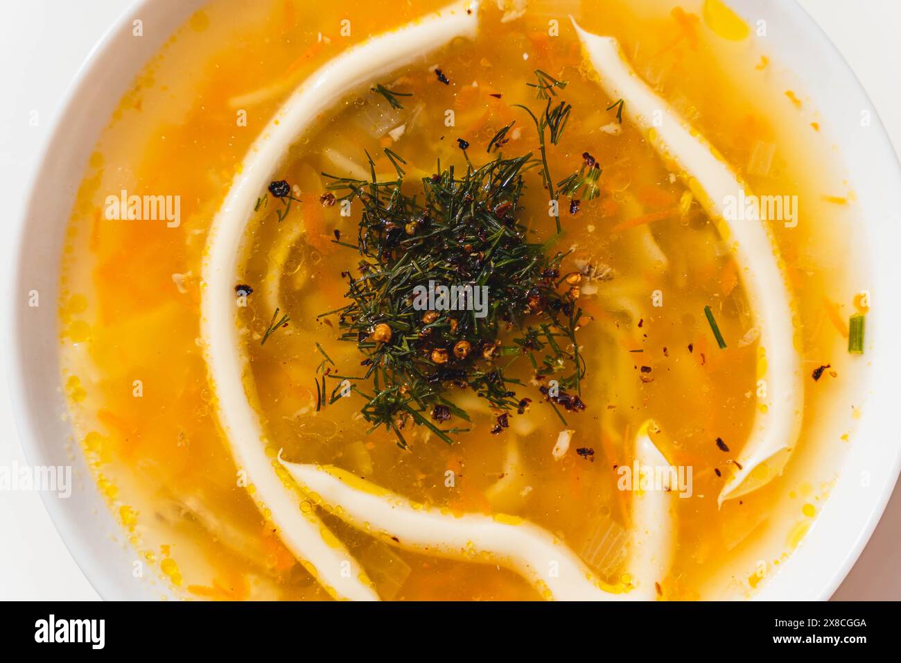 Eine weiße Schüssel gefüllt mit köstlicher Hühnersuppe garniert mit Kräutern und Mayonnaise. Stockfoto